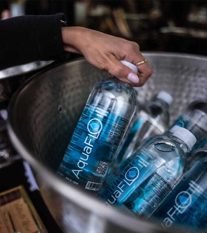 A hand lifting an AquaFlo bottle out of a metal ice bucket