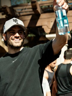 A man in a cap raising an AquaFlo bottle at an outdoor event